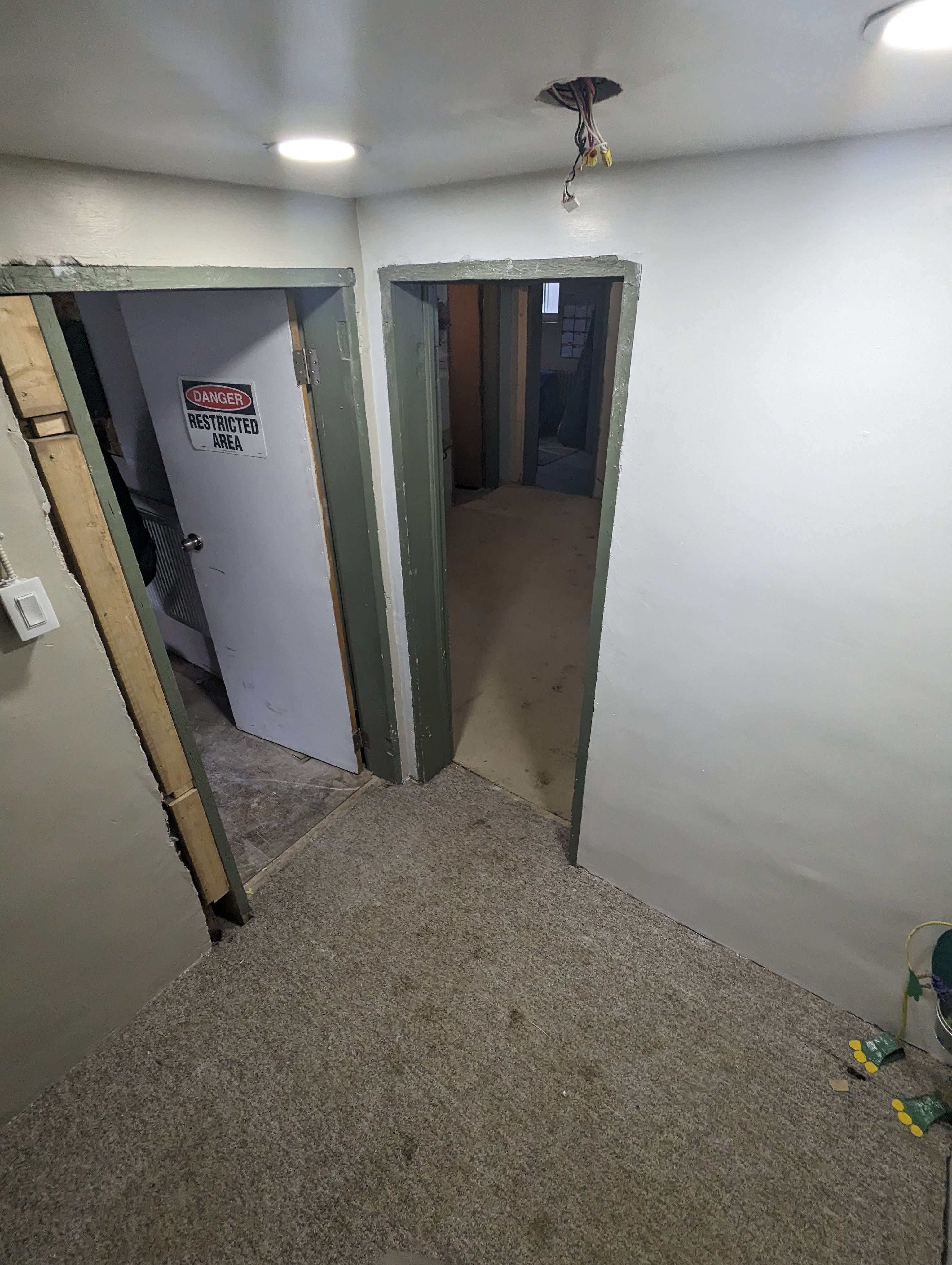 Unfinished basement hallway with danger sign, rough walls, exposed wiring