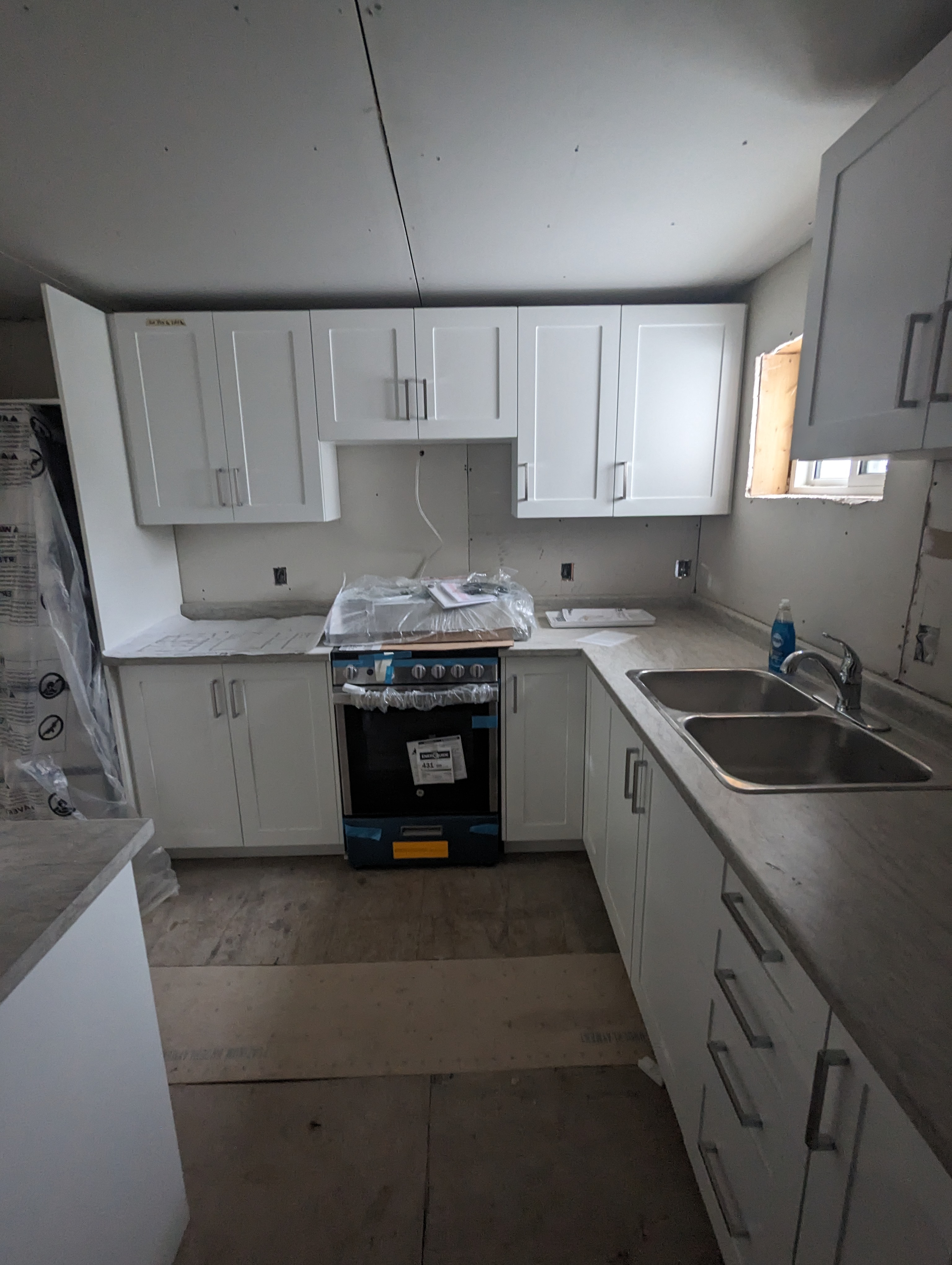 Basement kitchen during construction, drywall and cabinets being installed, lumber stacked